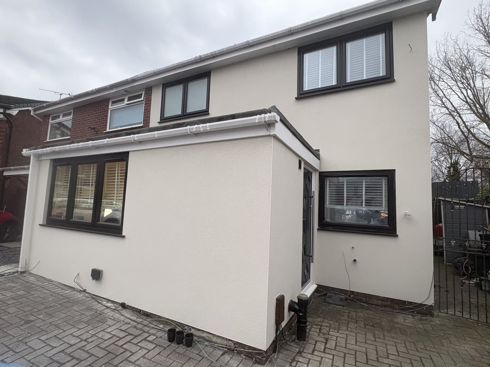 Two-storey house finished in cream monocouche render, with dark grey window frames and block paving